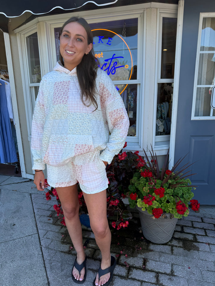 Person wearing quilted hoodie sweatshirt and matching quilted drawstring shorts in pastel pink and blue stripes and floral quilting square patterns.