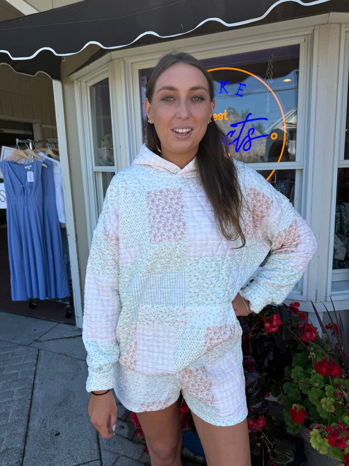 Person wearing quilted hoodie sweatshirt and matching quilted drawstring shorts in pastel pink and blue stripes and floral quilting square patterns.