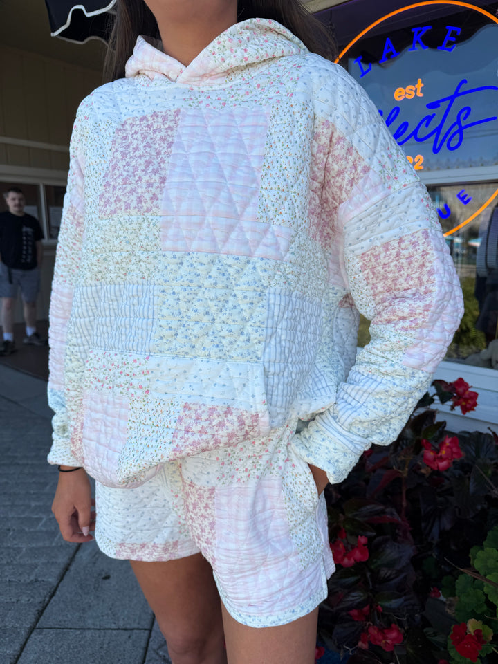 Person wearing quilted hoodie sweatshirt and matching quilted drawstring shorts in pastel pink and blue stripes and floral quilting square patterns.