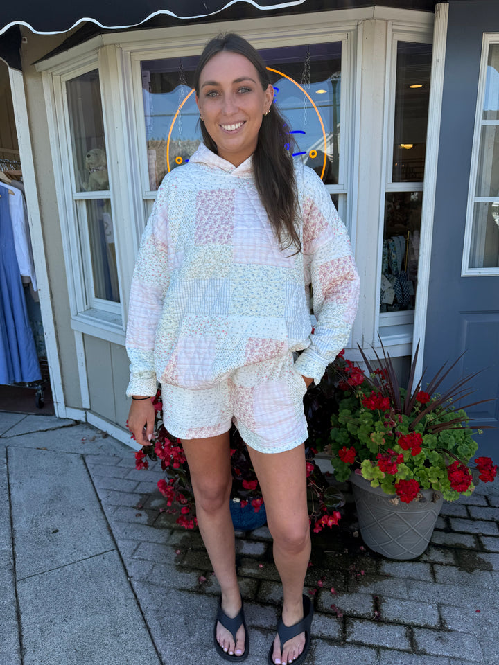 Person wearing quilted hoodie sweatshirt and matching quilted drawstring shorts in pastel pink and blue stripes and floral quilting square patterns.