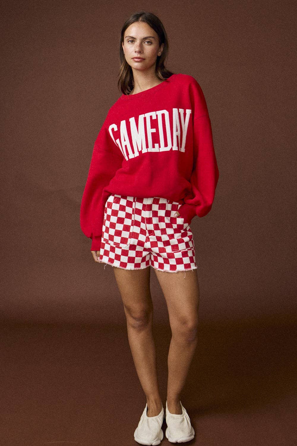 Person wearing a red 'GAMEDAY' sweatshirt and red and white checkered shorts on a brown background