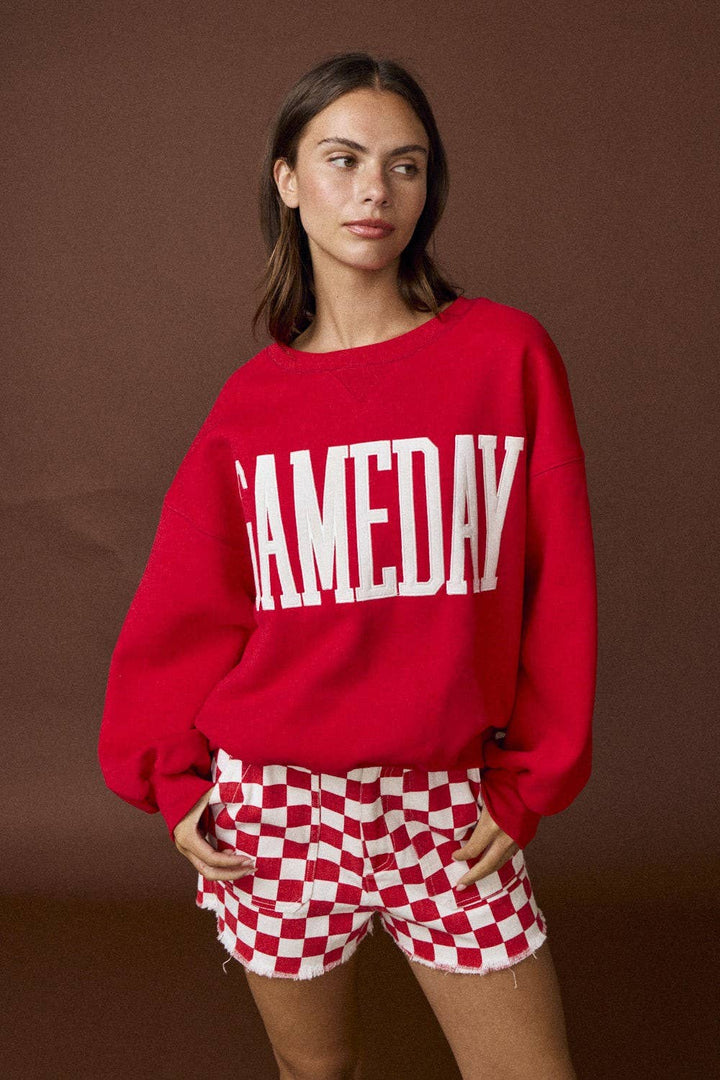 Person wearing a red sweatshirt with 'GAMEDAY' text and checkered shorts on a brown background