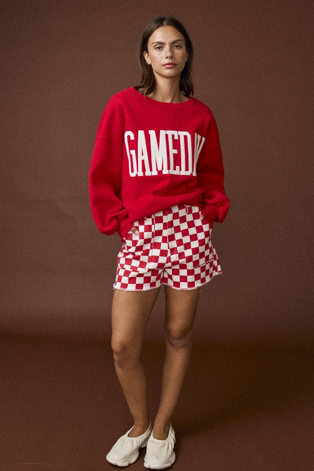 Person wearing a red sweater with 'GAMEDAY' text and red and white checkered shorts on a brown background