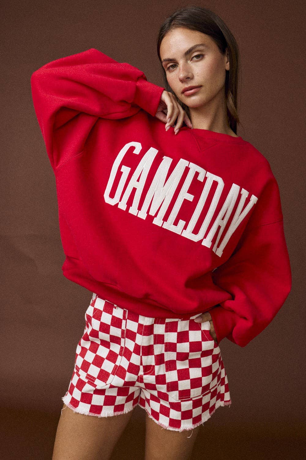 Person wearing a red 'GAMEDAY' sweatshirt and checkered shorts on a brown background
